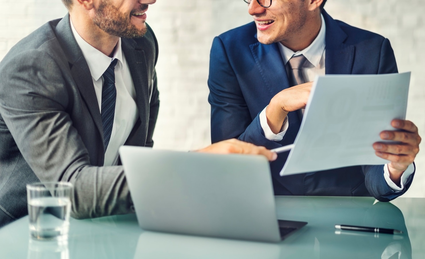 Two professional man talking to each other sitting at a table with a laptop